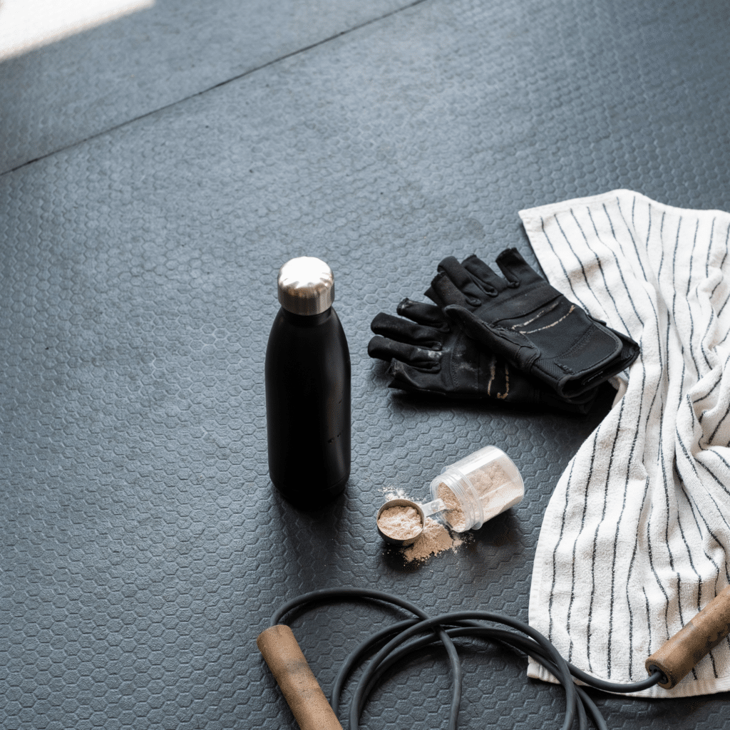 Flat lay of water bottle, towel, and electrolytes on gym floor